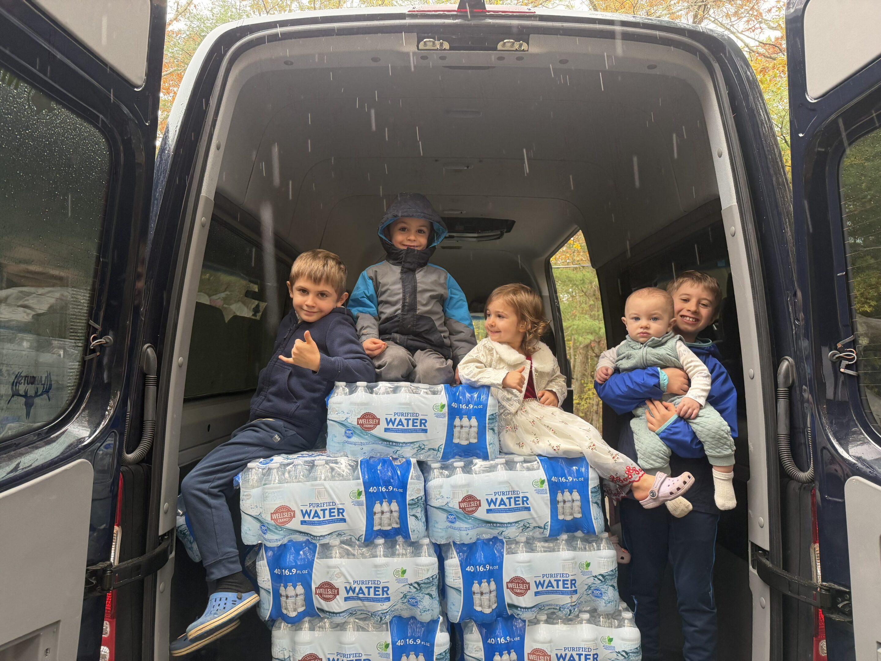 A group of children sitting in a vehicle surrounded by bottled water packs.