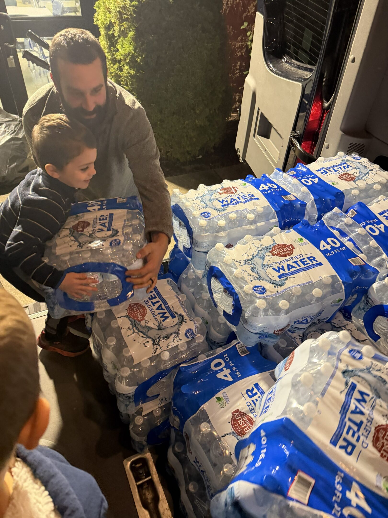 A man and child holding a large pack of toilet paper rolls.